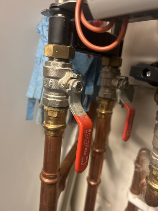 Avstängningsventiler med röda handtag och kopparrör, del av ett rörsystem för fjärrvärmecentral.