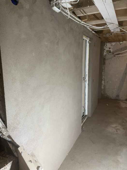 Putsad vägg i ett rum under renovering, även tak och golv syns.