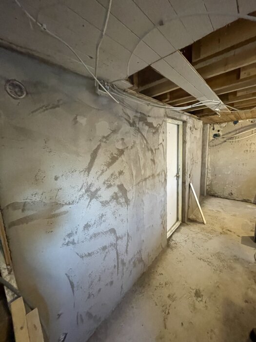 En vägg putsad med Combimix putsbruk, visar olika lager av puts i en renoveringssituation. Tak och dörrkarm syns också.