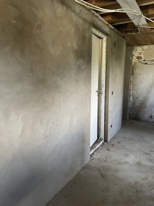 Putsad vägg inomhus i ett renoveringsprojekt med en dörr och exponerade takbjälkar.