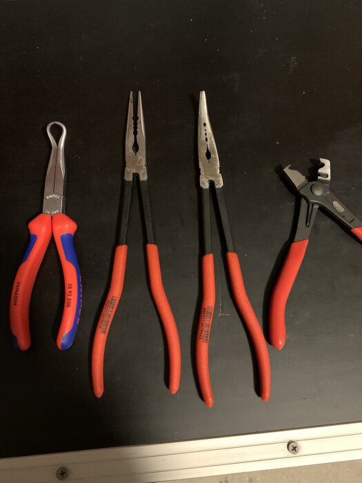 Flera tänger med röda handtag på ett svart underlag.