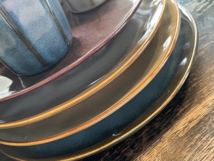 Staplade, färgglada tallrikar med en blå kopp ovanpå mot en mörk träyta.