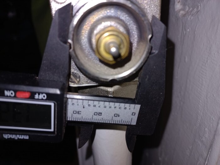Närbild av en termostatventil på en radiator mätt med ett digitalt skjutmått, som visar ventildiametern.
