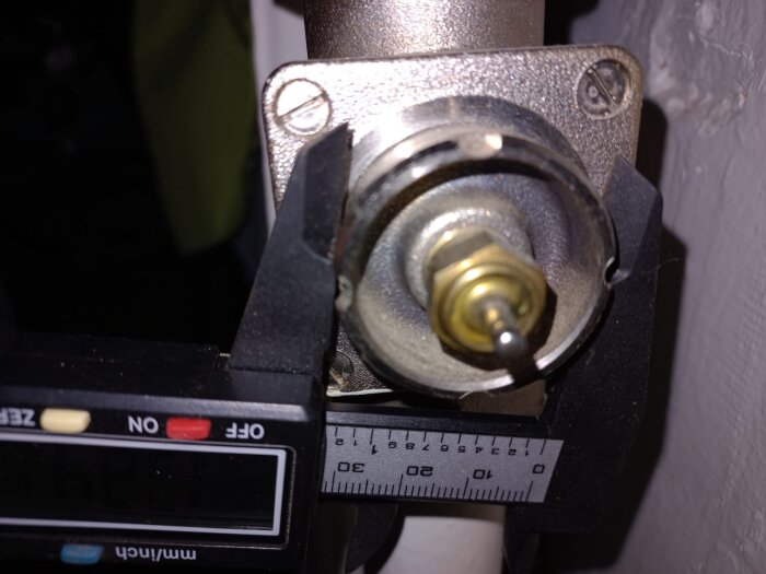 Mätverktyg mäter diameter på en ventilanslutning på en radiator utan termostat i ett gammalt hus.