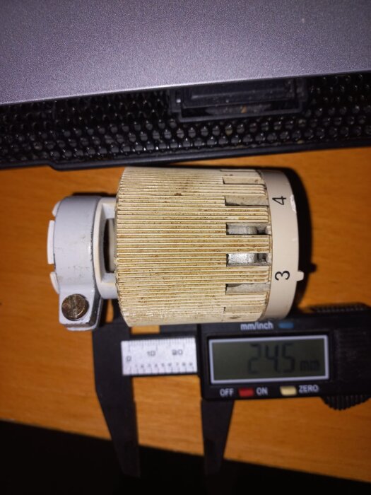Termostat från radiator med mätskjutmått visar diameter på 24,5 mm i gammalt hus, monterad på träbord.