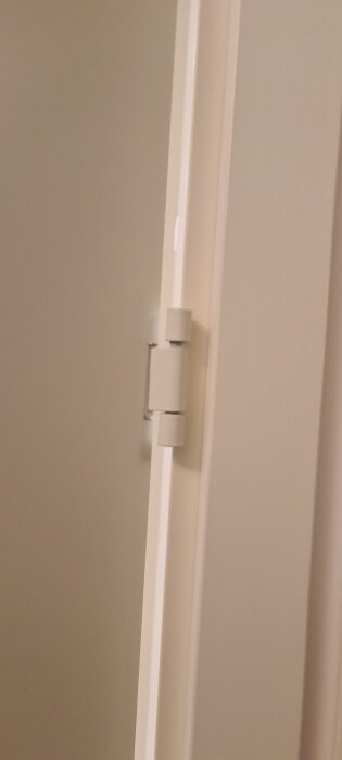 Övre gångjärn på en vit innerdörr och dörrkarm som verkar kräva justering.