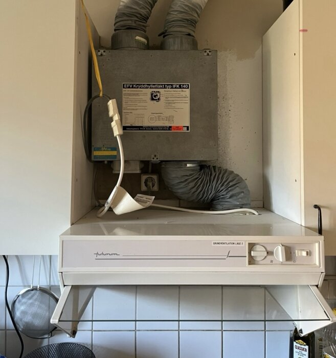 Vit Futurum spiskåpa med två vred och lysknapp i kök, EFV kryddhyllefläkt IFK 140 i överskåp ovanför, synliga röranslutningar.