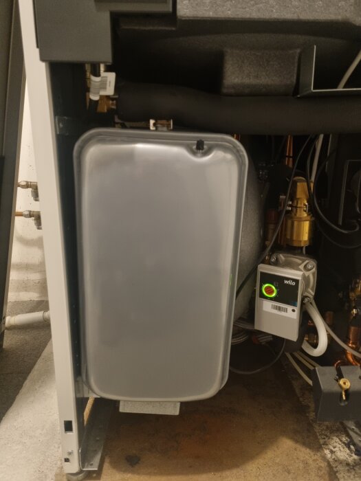 Närbild av insidan av en värmepump eller liknande enhet med en grå expansionstank och en digital LED-display från märket Wilo.