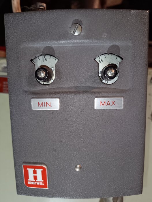 Äldre Honeywell-termostat med två rattar för minimi- och maxtemperaturinställning och en röd Honeywell-logga nederst.