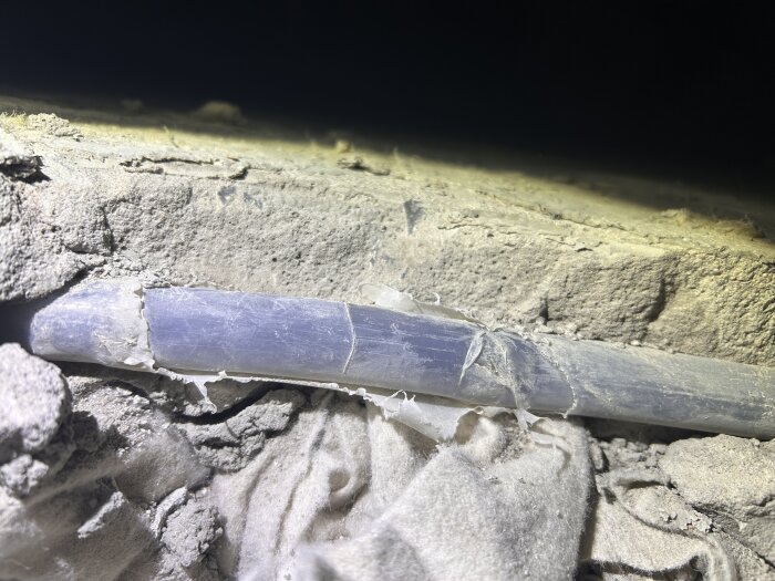 Närbild på skadad slang för vattenburen golvvärme med jack i plasten, omgivet av byggdamm och betong.