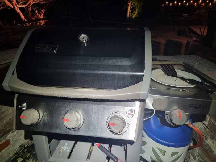 Gasolgrill vid kvällstid med stängd huv och gasolflaska, redo att användas för att grilla hamburgare.