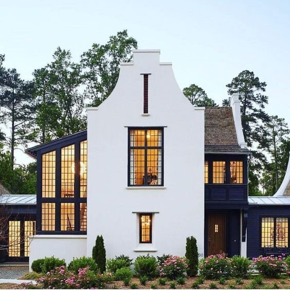 Klassiskt hus med vit fasad och stora fönster, omgiven av träd och grönska.