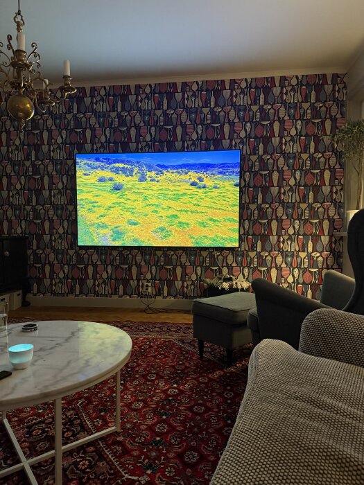 TV monterad på mönstrad vägg i vardagsrum, visande landskapsbild.