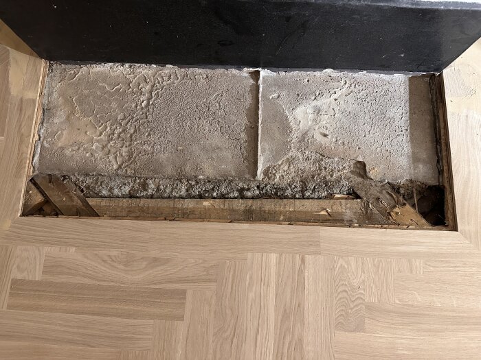 Golv med öppning för kalkstensskiva, ojämn botten, omgiven av trä och träimitationsplattor, redo för installation.