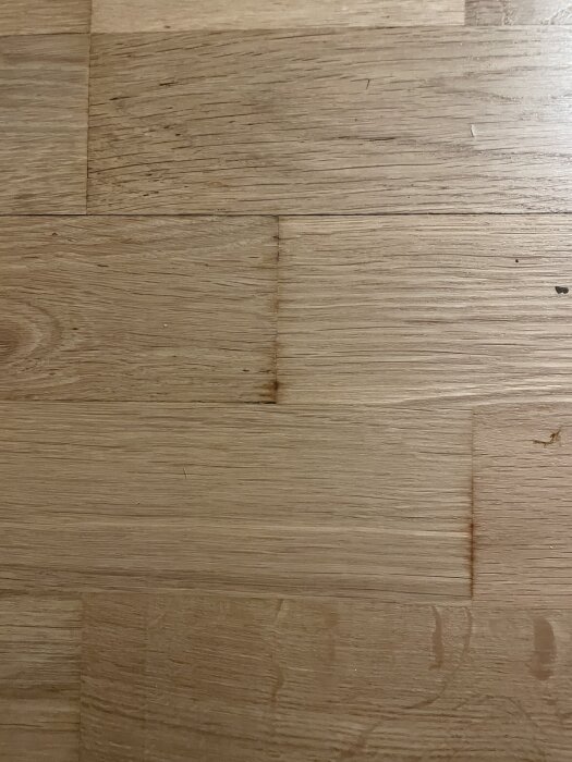 Slipat och lackerat trägolv med ojämnheter och färgskiftningar mellan plankorna, eventuellt resultat av professionell behandling.