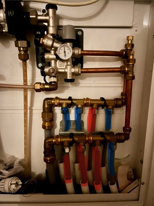 Uppvärmningssystem med kopparrör och tryckmätare; rör märkta med röda och blå färger, några varma och andra kalla.