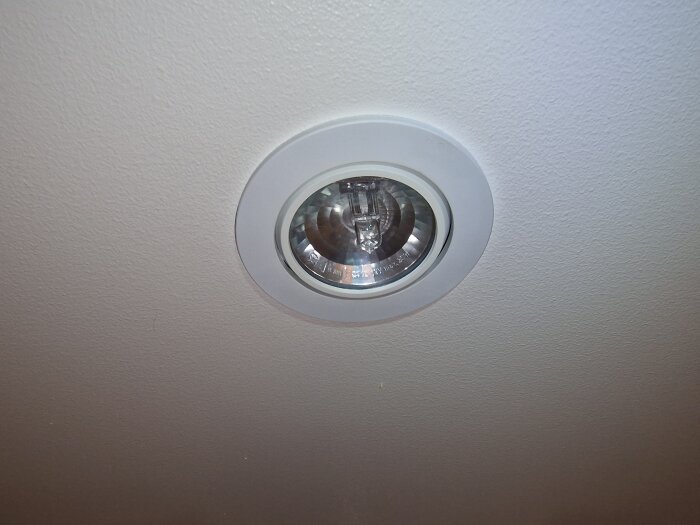 Inbyggd vinklingsbar spotlight i tak utan synlig ring för lamputtag, omgiven av vit fastsatt ring.