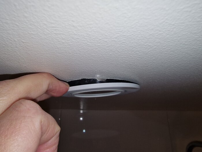 Hand drar i vinklingsbar spotbelysning i taket, osäker på hur lampan byts ut.