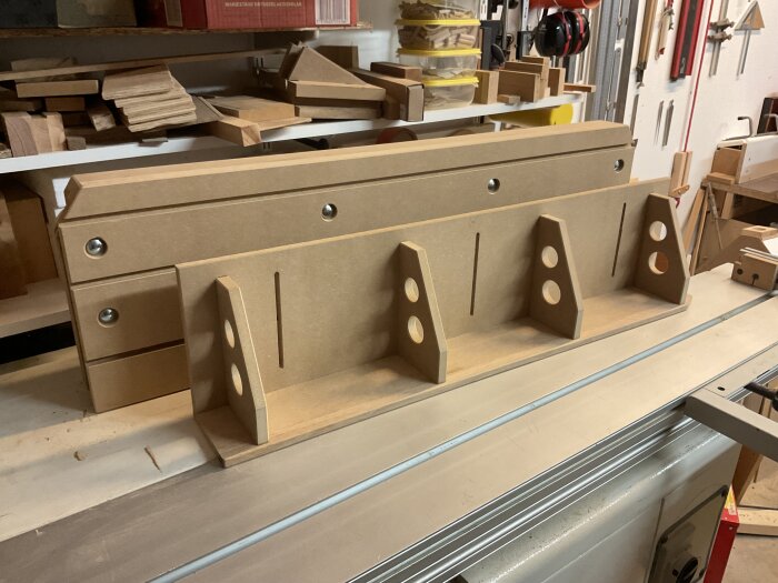 MDF-konstruktion i vinkel, med urfrästa hål, placerad på en arbetsbänk i verkstadsmiljö.