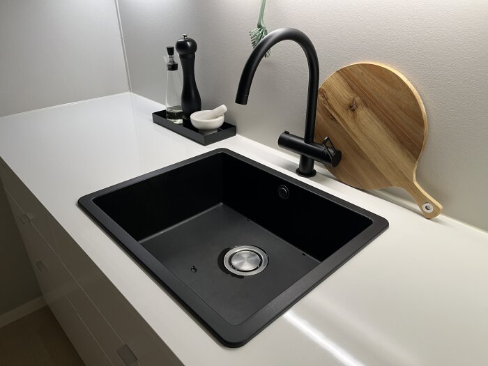 Svart diskho med modern kran, skärbräda och kryddor i ett välskött kök.