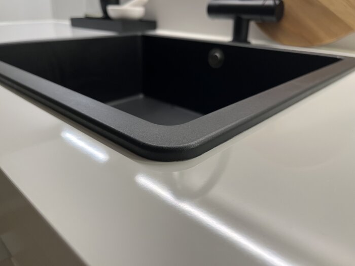 Svart diskho i ett modernt kök med ett stilrent, reflekterande köksbänksskiva vid sidan.
