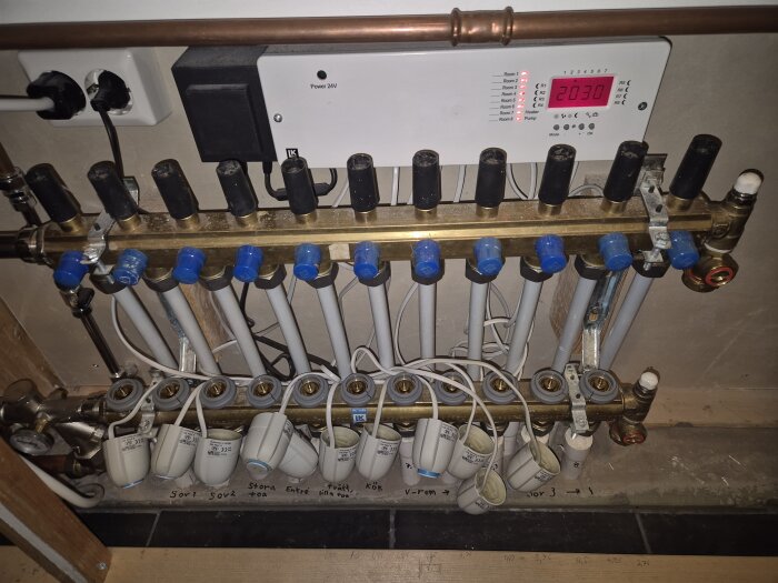 Rörsystem med flera anslutningar och reglage, en panel med digital display syns ovanför. Finns i diskussion om maxtermostat för golvvärme.