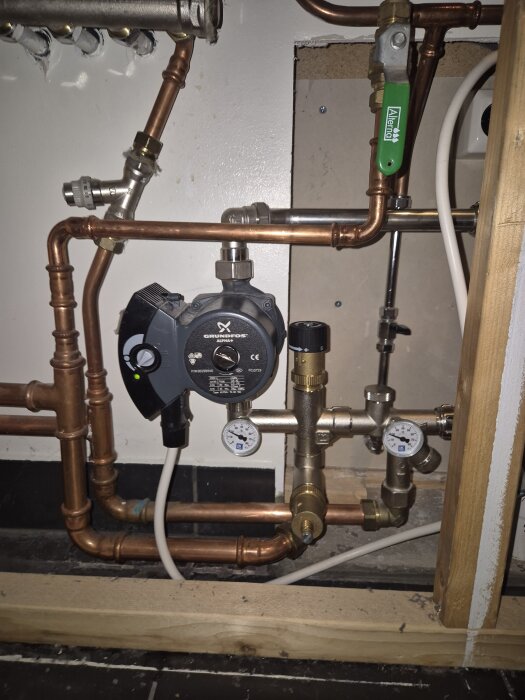 VVS-system med kopparrör, ventiler och en Grundfos-pump visas. Två tryckmätare och en grön ventil är synliga.