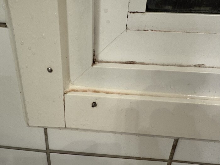 Fönsterkarm nära dusch med våt yta och rostfärgad silikonfog. Smutsig skarv mellan karmens delar.