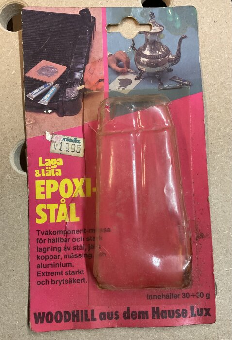 Förpackning av "Epoxi-Stål" från Laga & Låta med plastöverdrag, etikett med pris 19,95 kr, beskriven som tvåkomponent-massa för reparation av metaller.