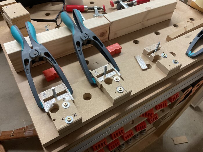 Frästa gjutformar av MDF med packtejp, M6-skruvar på plats, hålls fast av svarta klämmor på en arbetsbänk i verkstaden.