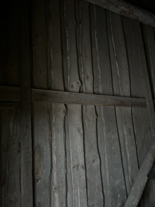 Innervägg med okantade brädor i ett vedlider, möjligtvis tidigare yttervägg, diskuterad för sin byggnadsteknik från 1700-talet.
