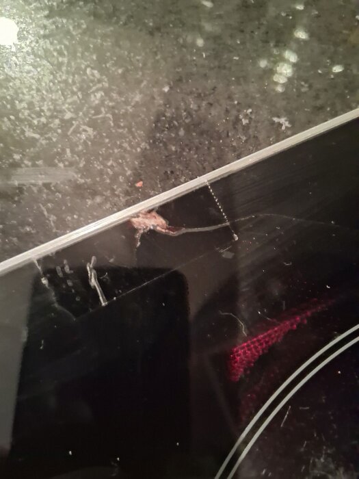 Närbild på en induktionshäll med en krosskada och sprickor i glaset nära kanten.