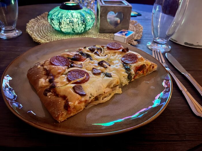 Pizza slice on a plate with salami, pork fillet, onion, pesto, tomato, and cheese.