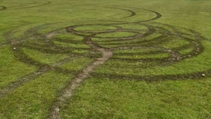 Mönster av cirklar i gräset skapat av en fyrhjuling, visar däckmärken på en stor gräsyta.