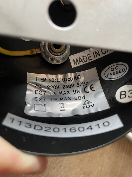 Etikett inuti en lampa visar specifikationer: ITEM NO: LI150700, 220V-240V, 50Hz, max 60W, tillverkad i Kina, QC-passerad, E27-sockel.