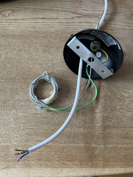 Insida av lampbas med kablar och en metallfäste liggande på träbord, innehåller text 'MADE IN CHINA' synlig på etiketten.