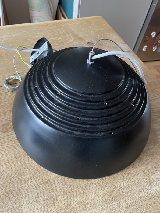 Svart rund lampskärm på ett bord med synlig sladd och monteringstillbehör.