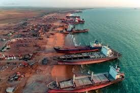 Flera stora fartyg ligger uppdragna på en strand, sannolikt en skeppskyrkogård, med havet i bakgrunden.