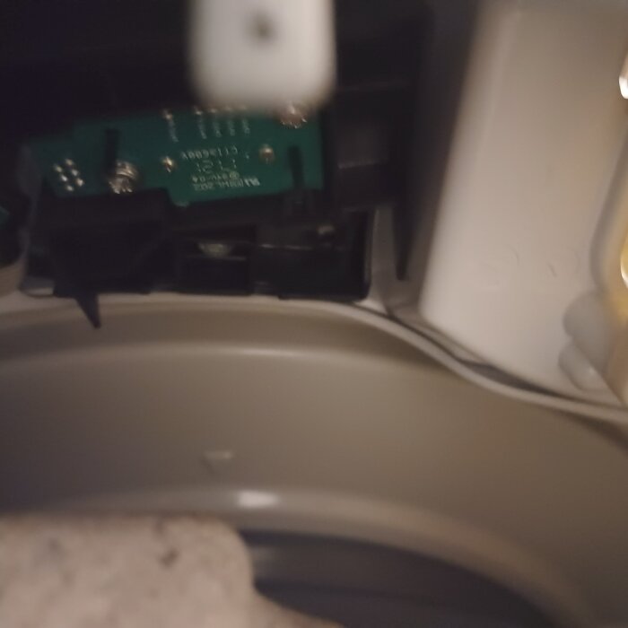Närbild av insidan på en hushållsmaskin, med synlig kretskort och kablar.