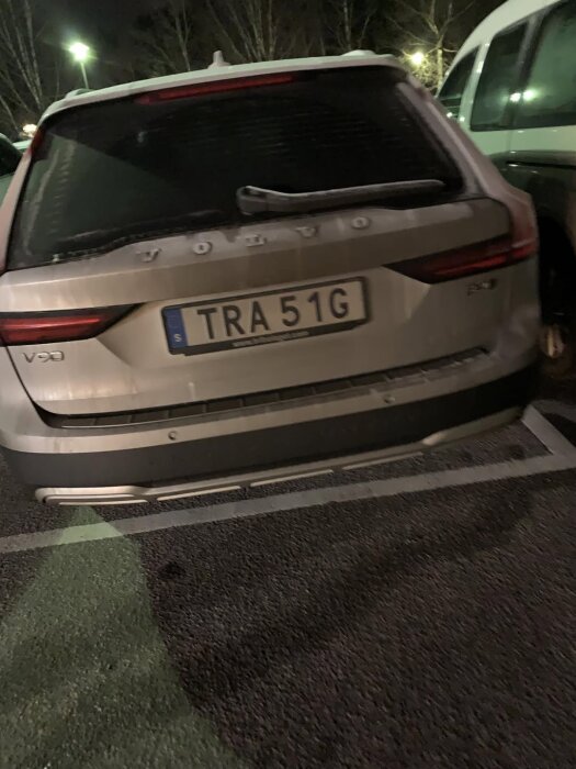 Bakre delen av en vit Volvo V90 parkerad utomhus på en mörk asfalterad yta, med registreringsskylten TRA 51G synlig.