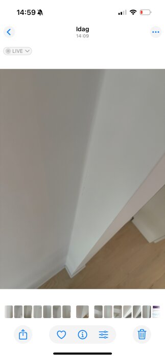 Spricka längs en vit vägg i hörnet av ett rum med träparkettgolv.