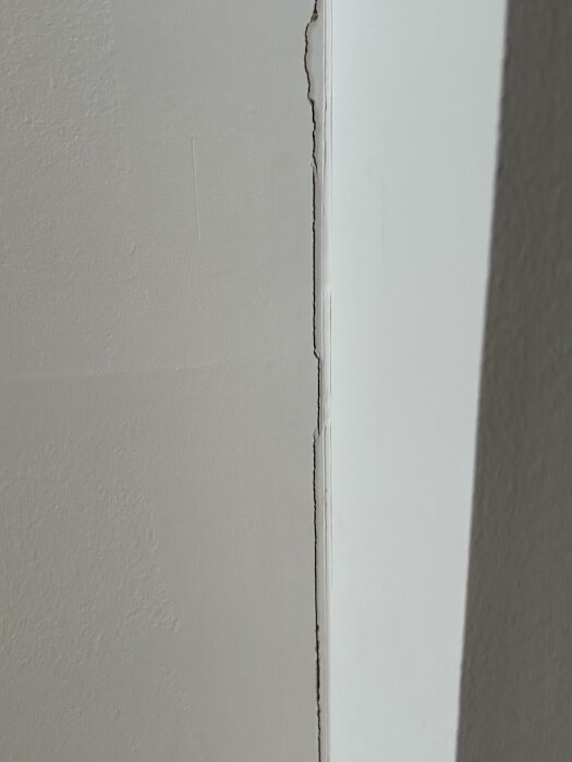 Spricka i en vitmålad vägg med synliga lager och ojämna kanter.