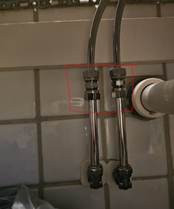 Två metallrör under handfat med förminskade anslutningar markerade i rött. Tilebeklädd vägg i bakgrunden.
