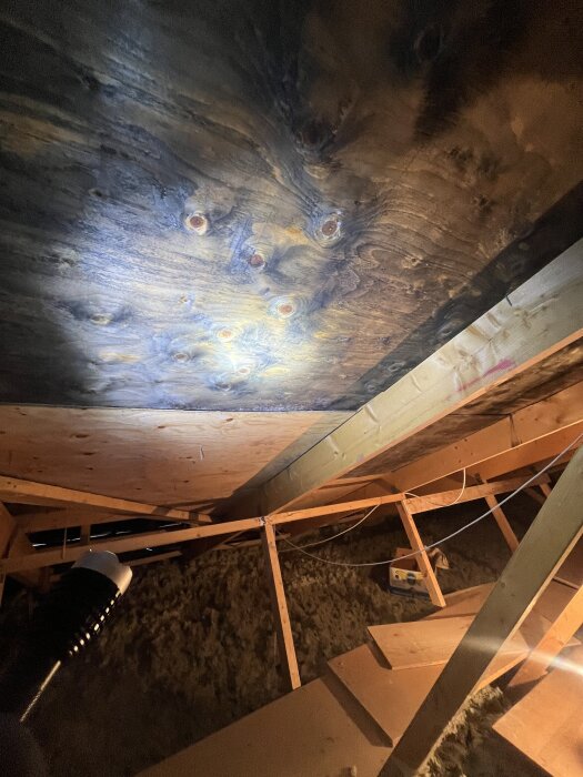 Mörka träfiberskivor på en vind med påväxtliknande mönster; skillnad synlig mellan skivorna.