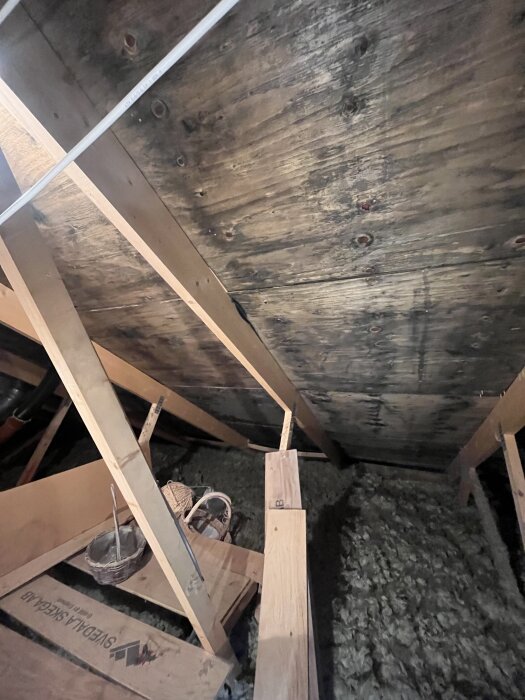 Mörka träfiberskivor på en vind i Myresjöhus, varierande i färg, med träreglar och några verktygslådor kring skivorna.