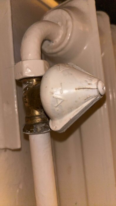 Närbild på en vit, gammal termostatventil på ett elementrör, med slitage och märken.