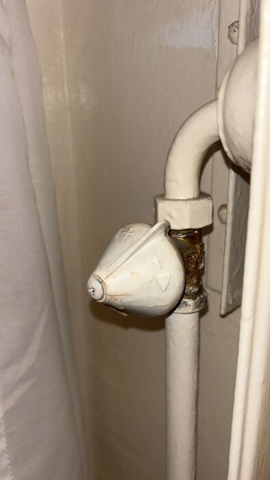 Vitt elementvred på ett rör, med rostfläckar runt fästet. Vredet misstolkas, läcker vatten vid justering.