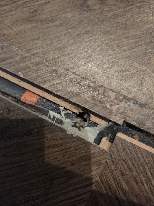 Lös övergångslist med skum och lim mellan två rum, synligt hål i gammalt betonggolv, delvis avlägsnade materiallager.