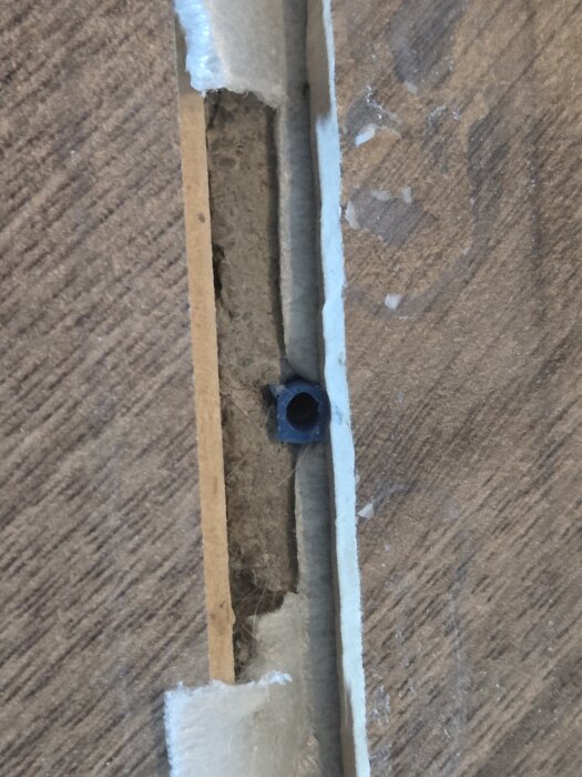 Övergångslist mellan rum med skruvhål ur bruk, exponerar betongunderlag från 60-talet, visad med trasigt lager och skum/lim-rester.