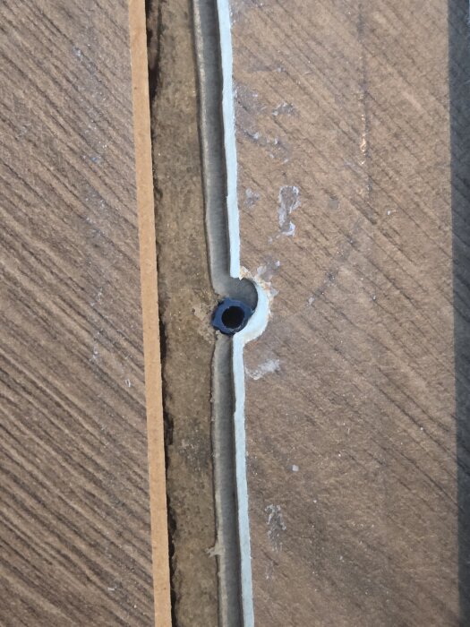 Övergångslist mellan två rum med synligt hål där skruv saknas, omgiven av gammal golvbeläggning och betongunderlag.